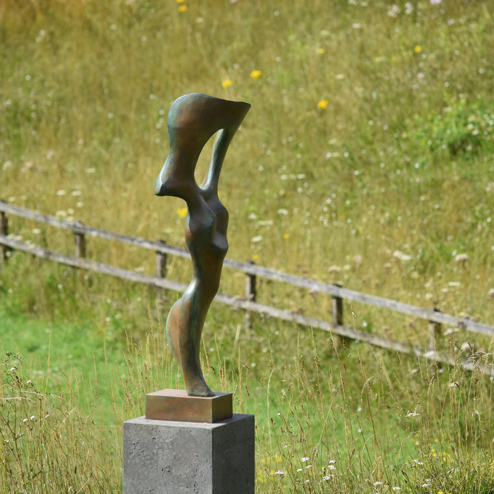 Abstract bronze sculpture of a stylised female torso with flowing curves and a hollowed circular form near the head, displayed in various outdoor and indoor settings. The sculpture has a rich patinated surface with green, gold, and bronze tones.