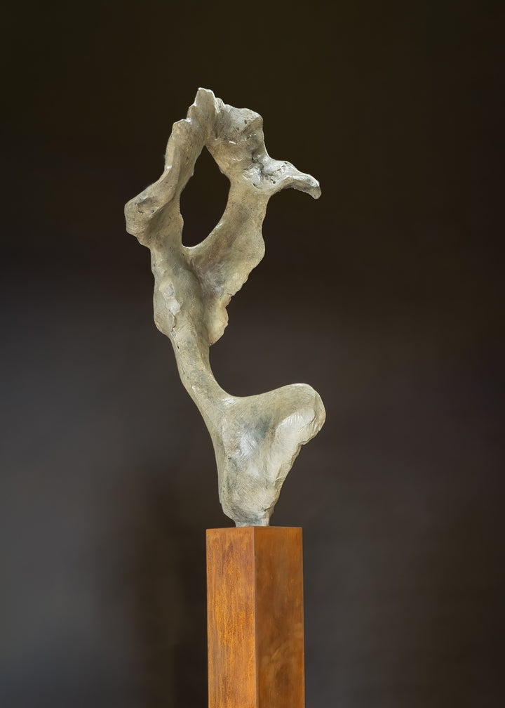Abstract bronze sculpture by Nicola Godden titled “Bone Form VI”, featuring an elongated organic form with a hollowed negative space near the upper section, inspired by skeletal and geological structures. The sculpture rises vertically from a tall rusted steel plinth, with a softly textured, patinated bronze surface that emphasises erosion, balance, and the quiet strength of natural forms within contemporary sculptural practice.