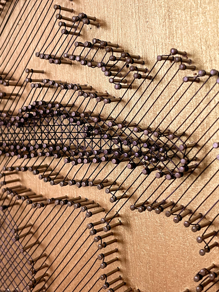 Portrait of David Bowie formed from fine black enamelled copper wire tensioned around thousands of small nails on a gold-toned board, with layered linear wiring defining facial features and hair through tonal contrast, depth and shadow across a textured metallic surface that shifts with light and viewing angle.