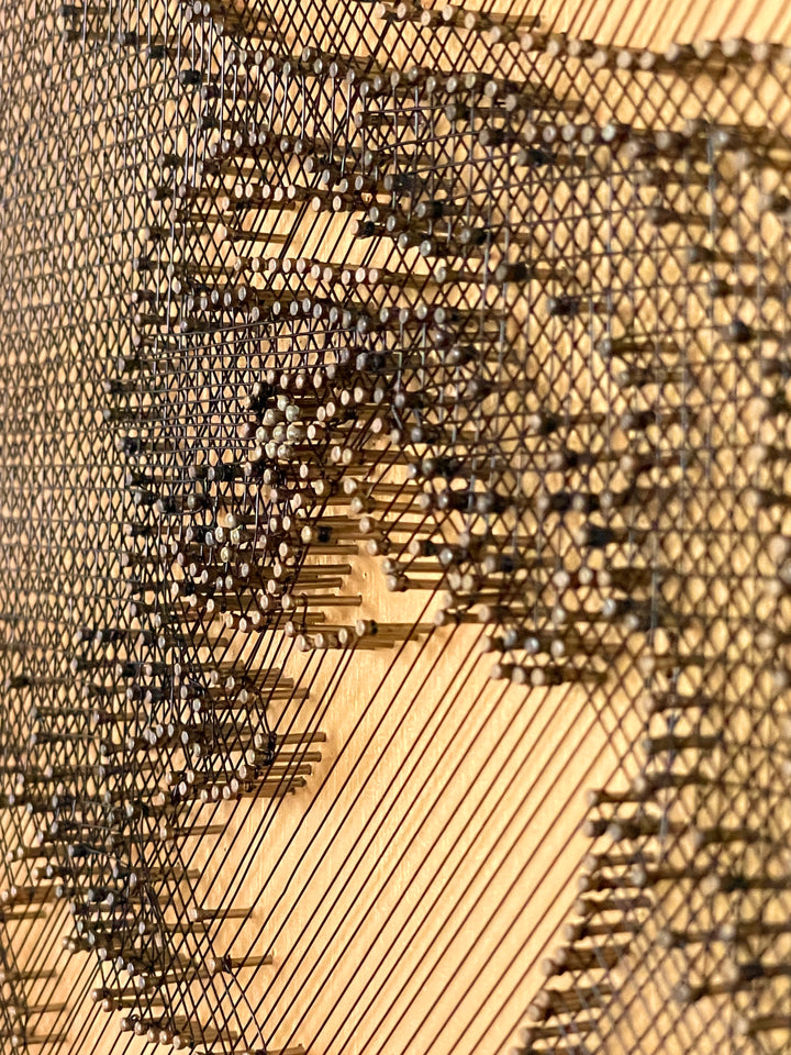 Portrait of David Bowie formed from fine black enamelled copper wire tensioned around thousands of small nails on a gold-toned board, with layered linear wiring defining facial features and hair through tonal contrast, depth and shadow across a textured metallic surface that shifts with light and viewing angle.
