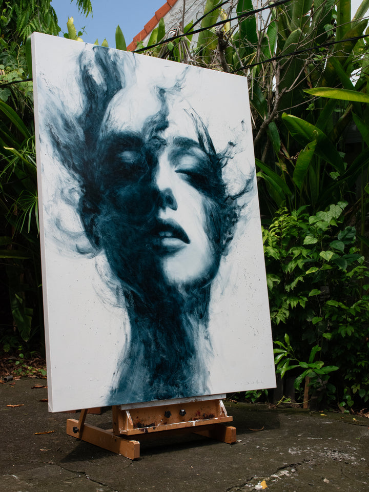 Large oil on canvas painting by Dan Bullock, titled Breathe. A monochrome portrait of a female face with eyes closed, emerging from swirling, smoky brushstrokes in deep teal and black against a pale background, balancing realism and abstraction.