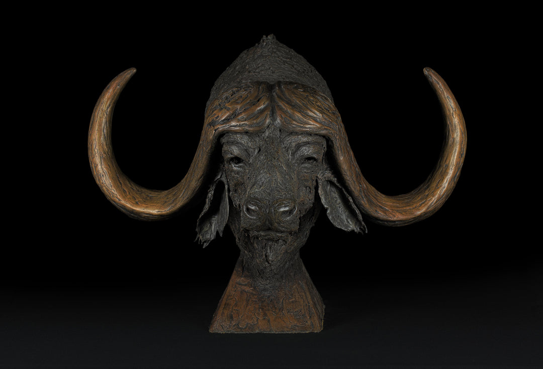 Textured bronze sculpture of a buffalo head with exaggerated, flowing horns and a rough, organic surface finish

