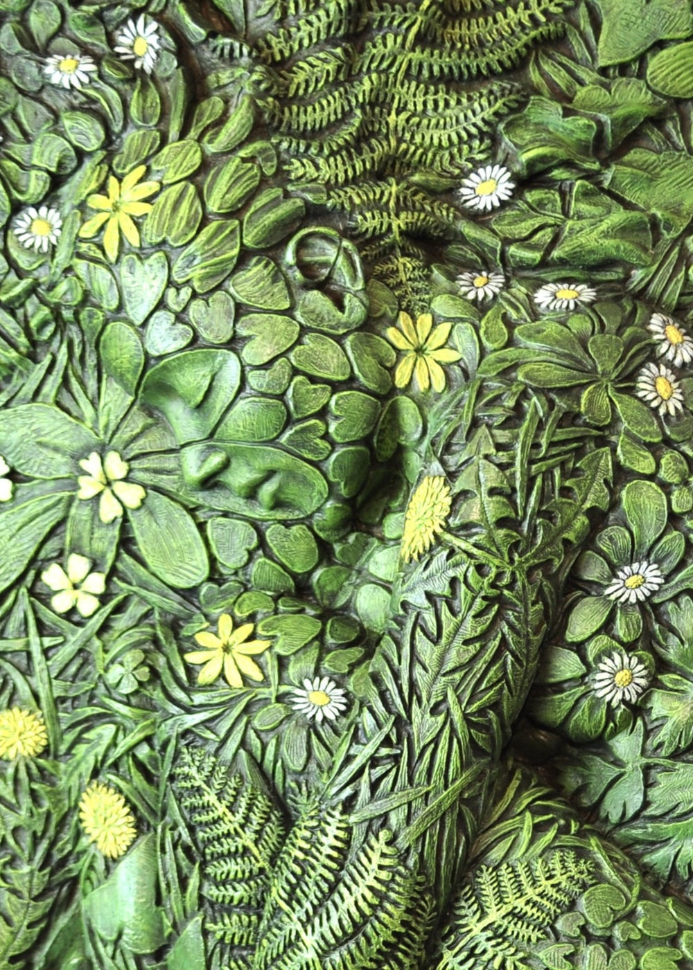 A hand-painted bronze bas-relief sculpture depicting a reclining female form emerging from dense spring foliage, with leaves, ferns and flowers flowing across her body, blending seamlessly into textured earth around the edge.