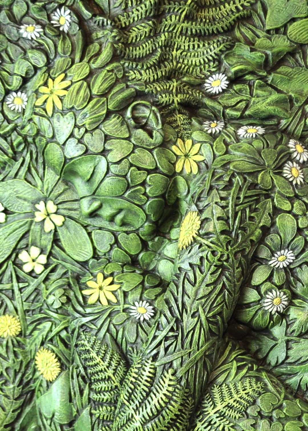 A hand-painted bronze bas-relief sculpture depicting a reclining female form emerging from dense spring foliage, with leaves, ferns and flowers flowing across her body, blending seamlessly into textured earth around the edge.