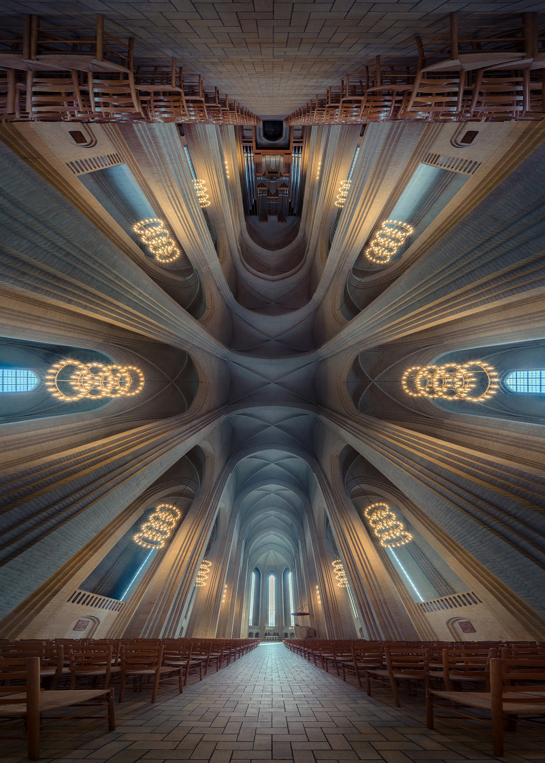Sweeping interior photograph of a cathedral with soaring brick arches, tall vertical windows, and glowing circular chandeliers blending with natural daylight, creating an ethereal sense of scale and calm.