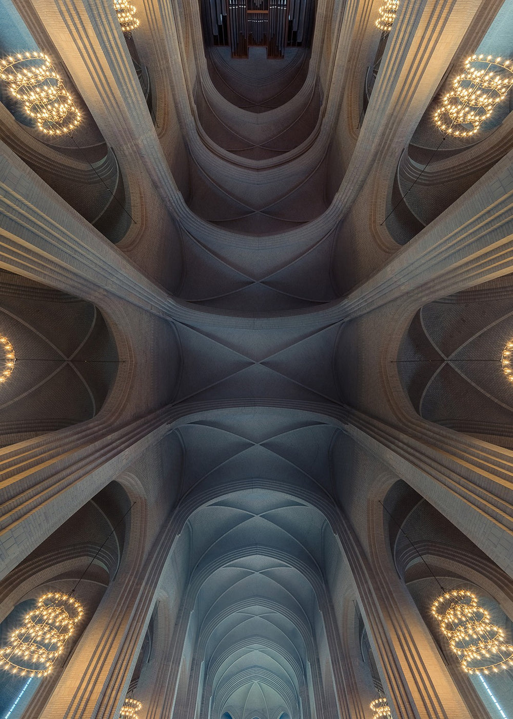 Sweeping interior photograph of a cathedral with soaring brick arches, tall vertical windows, and glowing circular chandeliers blending with natural daylight, creating an ethereal sense of scale and calm.