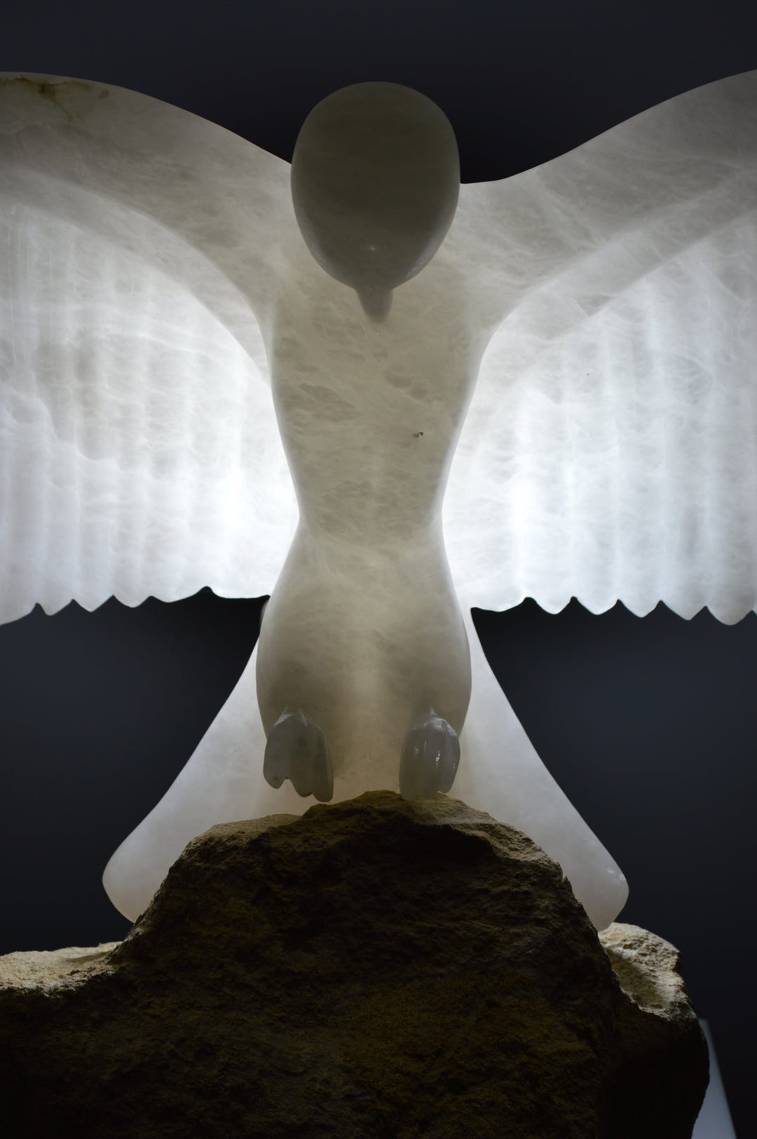 Deborah Harrison alabaster sculpture Caladrius, a translucent white bird with wide outstretched wings, finely carved feathers and smooth body, glowing with inner light on a rugged Farmington limestone base, symbolising purity, flight, and spiritual presence.