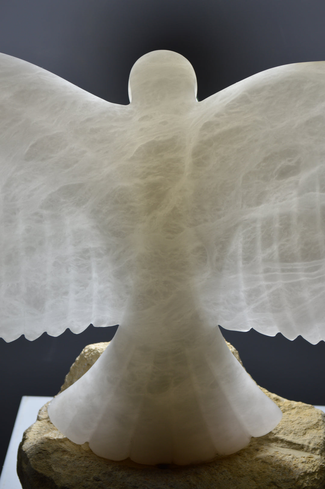 Deborah Harrison alabaster sculpture Caladrius, a translucent white bird with wide outstretched wings, finely carved feathers and smooth body, glowing with inner light on a rugged Farmington limestone base, symbolising purity, flight, and spiritual presence.