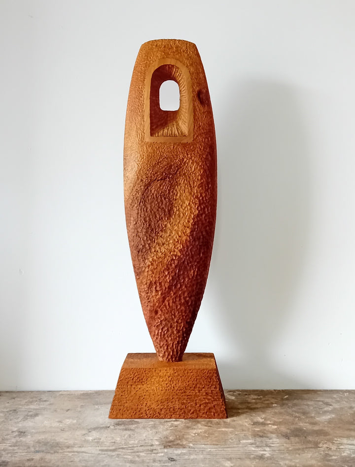 Nicola Beattie CAMINO sculpture — hand-carved cedar monolith with textured chisel-marked surface and arched window opening, symbolising a pilgrimage through life and a path towards hope. One-off original wooden artwork on cedar base.