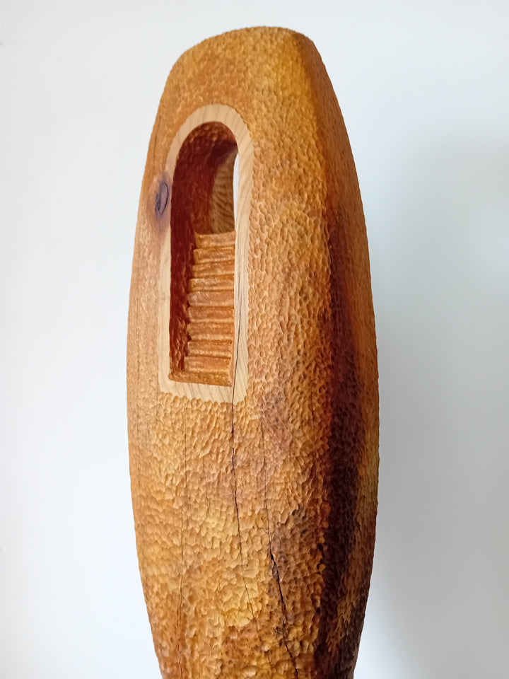 Nicola Beattie CAMINO sculpture — hand-carved cedar monolith with textured chisel-marked surface and arched window opening, symbolising a pilgrimage through life and a path towards hope. One-off original wooden artwork on cedar base.