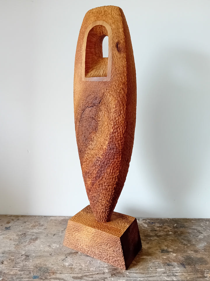 Nicola Beattie CAMINO sculpture — hand-carved cedar monolith with textured chisel-marked surface and arched window opening, symbolising a pilgrimage through life and a path towards hope. One-off original wooden artwork on cedar base.