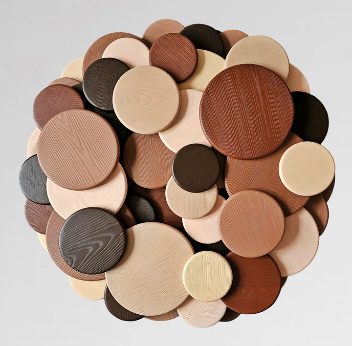 Wall sculpture made of layered wooden discs in various natural tones and wood grains, arranged in a circular cluster.

