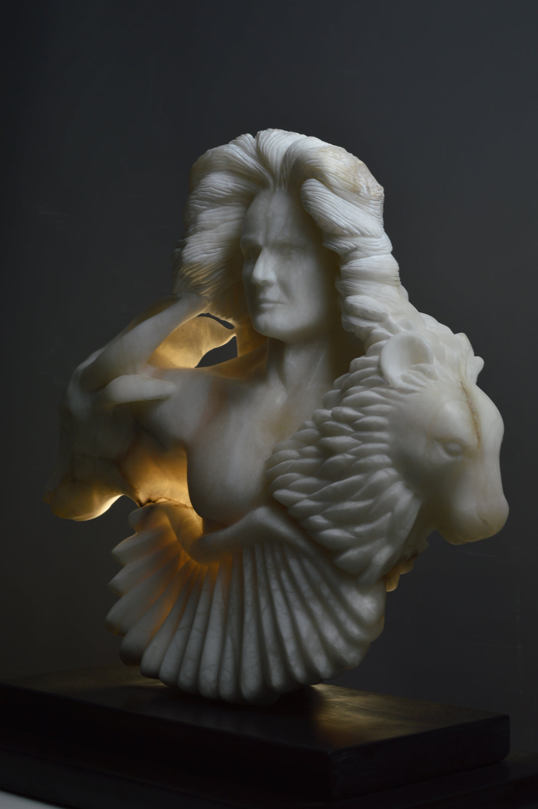 Deborah Harrison alabaster sculpture Cherubim, one-off hand-carved work in glowing white alabaster with translucent qualities, depicting a powerful male figure surrounded by symbolic forms including a goat-like animal, a bird, and a lion, mounted on slate, blending myth, spirituality, and masterful stone carving.