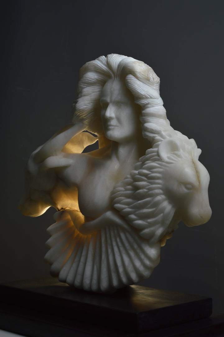 Deborah Harrison alabaster sculpture Cherubim, one-off hand-carved work in glowing white alabaster with translucent qualities, depicting a powerful male figure surrounded by symbolic forms including a goat-like animal, a bird, and a lion, mounted on slate, blending myth, spirituality, and masterful stone carving.