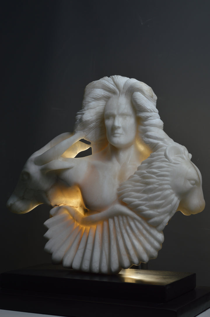 Deborah Harrison alabaster sculpture Cherubim, one-off hand-carved work in glowing white alabaster with translucent qualities, depicting a powerful male figure surrounded by symbolic forms including a goat-like animal, a bird, and a lion, mounted on slate, blending myth, spirituality, and masterful stone carving.