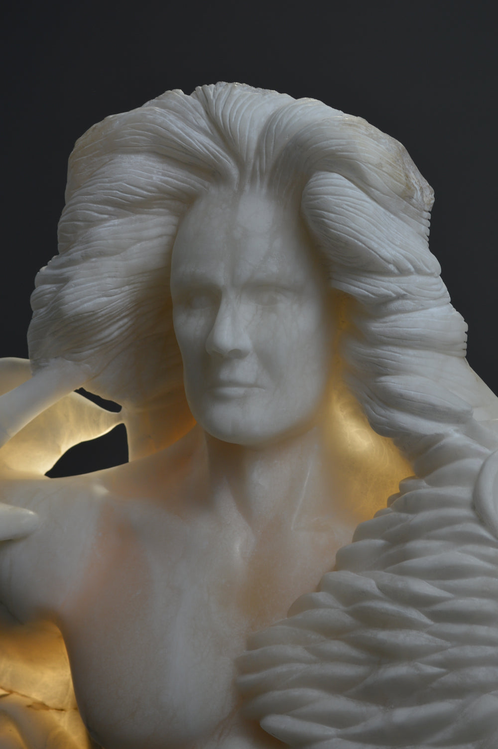 Deborah Harrison alabaster sculpture Cherubim, one-off hand-carved work in glowing white alabaster with translucent qualities, depicting a powerful male figure surrounded by symbolic forms including a goat-like animal, a bird, and a lion, mounted on slate, blending myth, spirituality, and masterful stone carving.