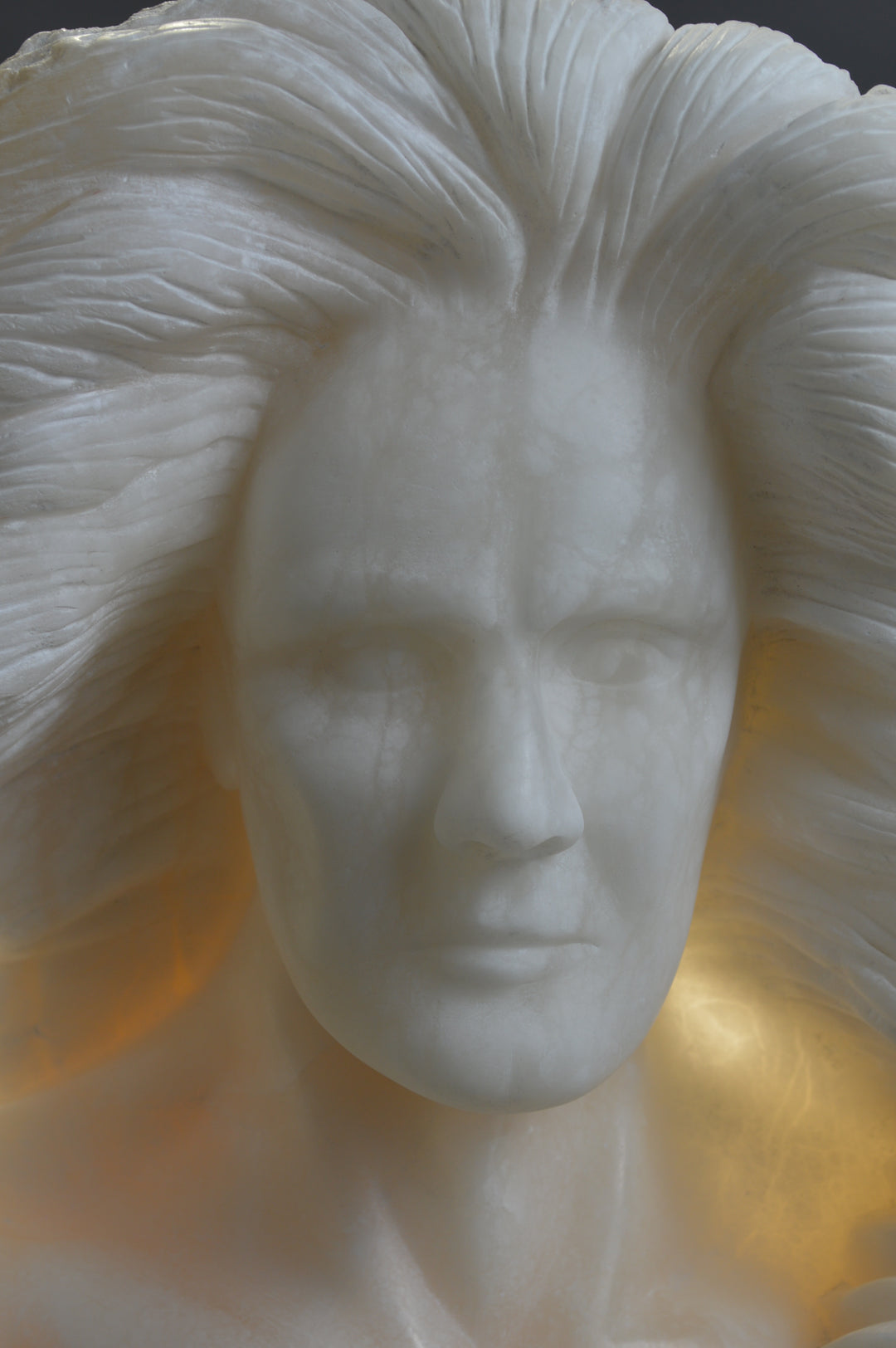 Deborah Harrison alabaster sculpture Cherubim, one-off hand-carved work in glowing white alabaster with translucent qualities, depicting a powerful male figure surrounded by symbolic forms including a goat-like animal, a bird, and a lion, mounted on slate, blending myth, spirituality, and masterful stone carving.