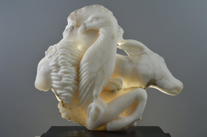 Deborah Harrison alabaster sculpture Cherubim, one-off hand-carved work in glowing white alabaster with translucent qualities, depicting a powerful male figure surrounded by symbolic forms including a goat-like animal, a bird, and a lion, mounted on slate, blending myth, spirituality, and masterful stone carving.