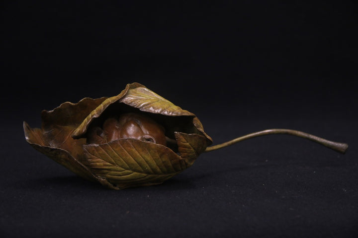 Bronze sculpture of a curled-up dormouse nestled inside a detailed horse chestnut leaf, with a long stem extending outward, set against a dark background.