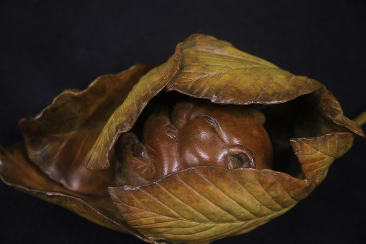 Bronze sculpture of a curled-up dormouse nestled inside a detailed horse chestnut leaf, with a long stem extending outward, set against a dark background.
