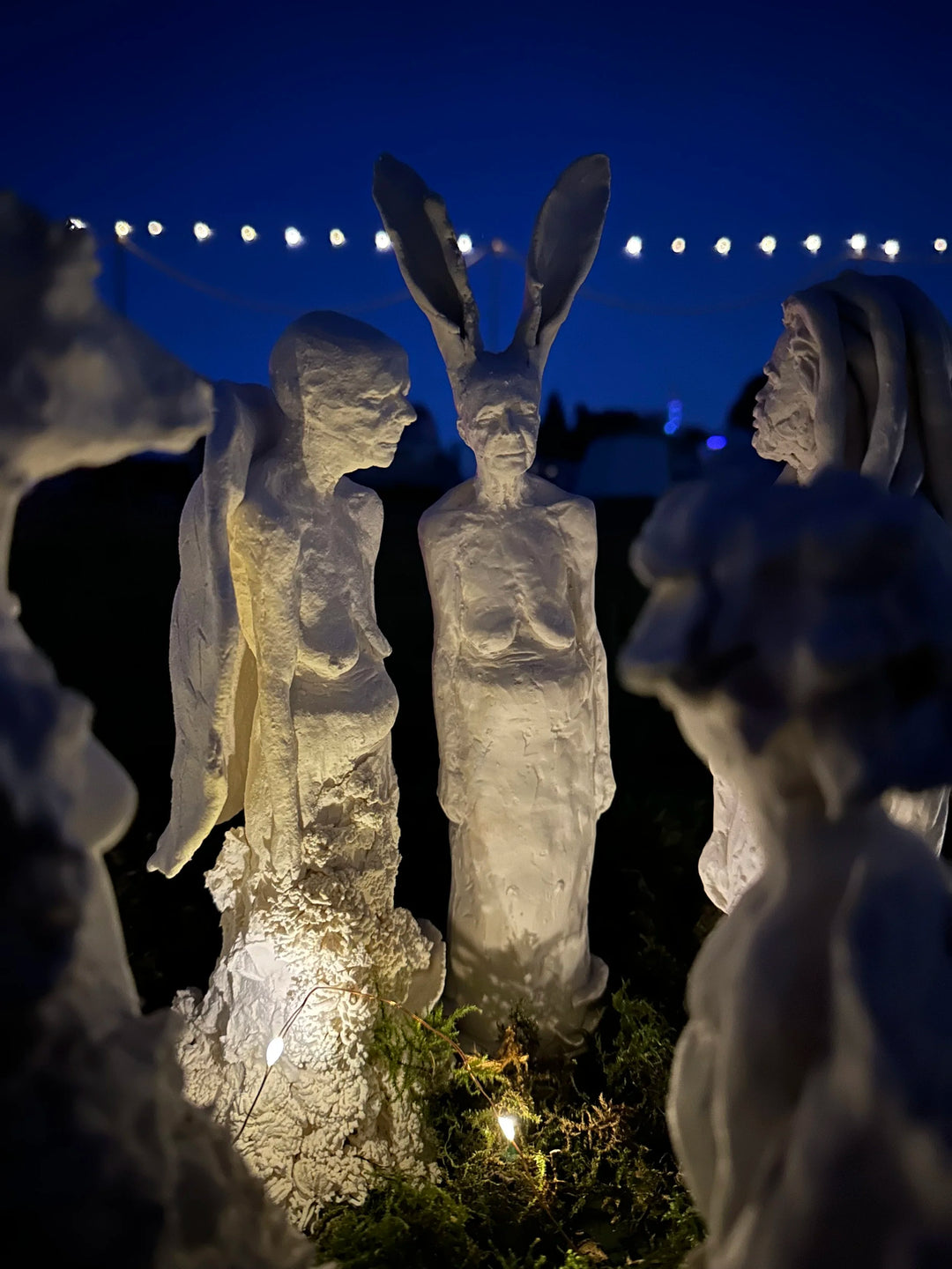 Eve Shepherd Children of Nature sculptural installation featuring around 100 individual porcelain hybrid figures combining human, animal, plant and fungal forms, arranged in a large illuminated fairy ring surrounded by natural moss.