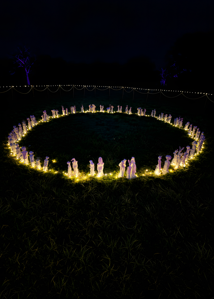 Eve Shepherd Children of Nature sculptural installation featuring around 100 individual porcelain hybrid figures combining human, animal, plant and fungal forms, arranged in a large illuminated fairy ring surrounded by natural moss.