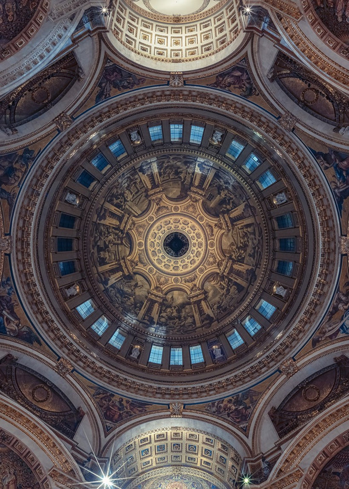 Panoramic photograph of St. Paul’s Cathedral interior, looking directly upward into the ornate dome designed by Sir Christopher Wren. The composition reveals gilded detailing, frescoes, marble arches, and the engineering mastery of the Whispering Gallery, captured in dramatic symmetry and ambient light.