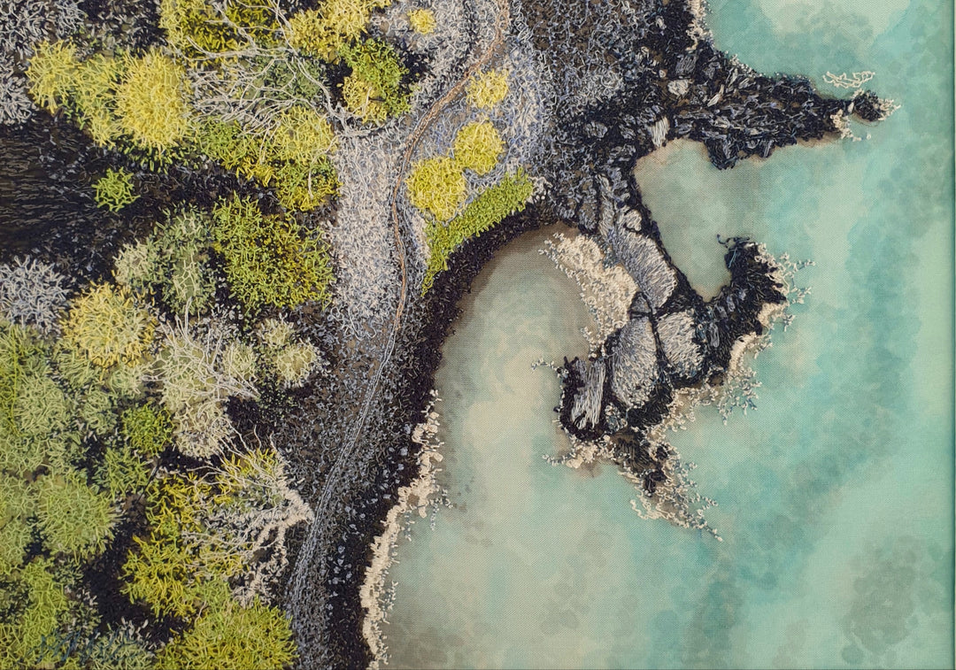 Aerial-style embroidered artwork of a rugged coastline with turquoise water, rocky textures, and mossy vegetation in shades of green and grey.

