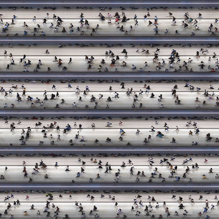 High-angle composite image of Hong Kong commuters moving through a brightly lit station, captured using high-speed video reconstruction. The figures are partially blurred and distorted, their faces downturned toward phones—creating a visual rhythm that blurs individuality, echoing the dehumanising pace of mass transit systems.