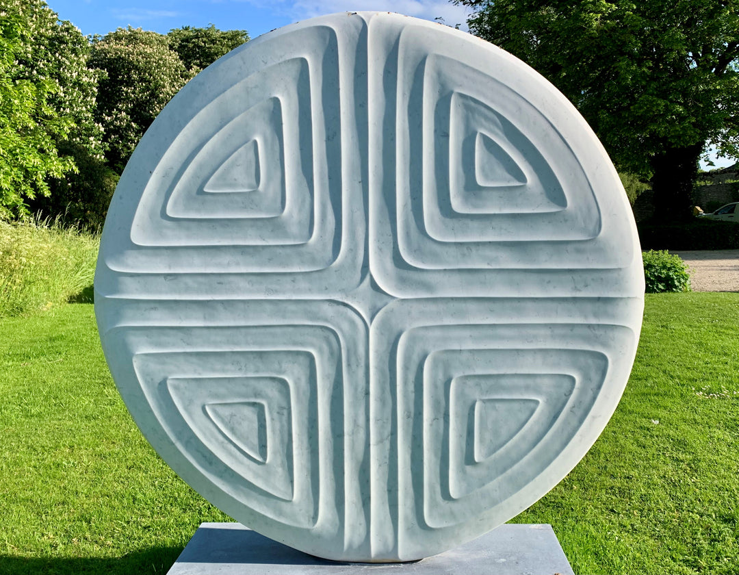 Contemplation V by Dominic Welch, a one-off Carrara marble sculpture with a circular form and four recessed triangular motifs, creating a harmonious, meditative design, currently exhibited at Ford Park Sculpture Garden.