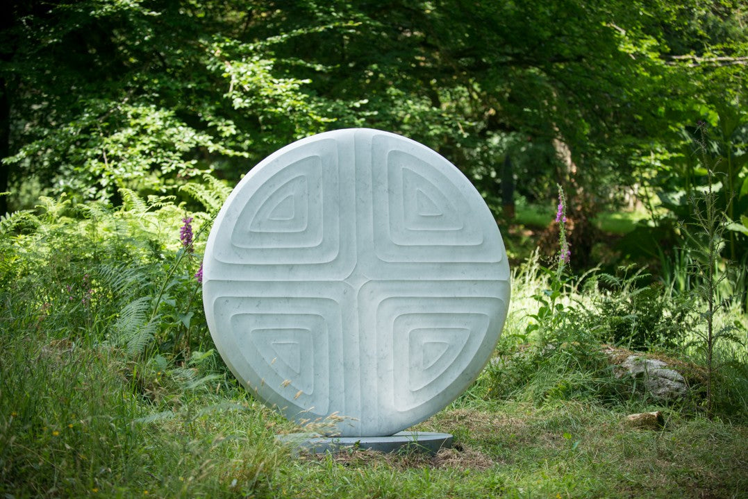Contemplation V by Dominic Welch, a one-off Carrara marble sculpture with a circular form and four recessed triangular motifs, creating a harmonious, meditative design, currently exhibited at Ford Park Sculpture Garden.