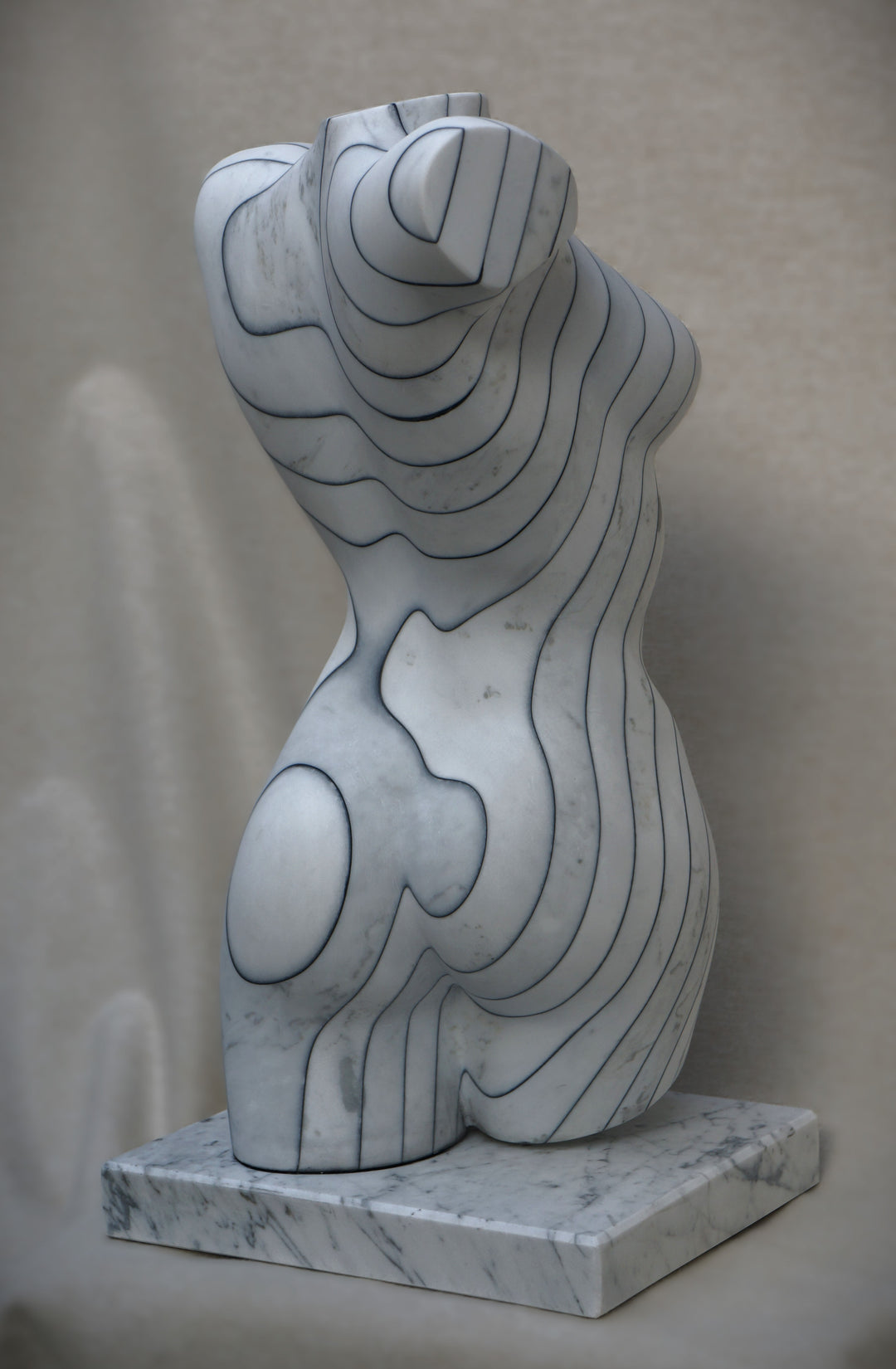 Contemporary marble sculpture of a female torso featuring engraved contour-like linework, mounted on a marble base, with a smooth, polished surface and subtle grey veining.