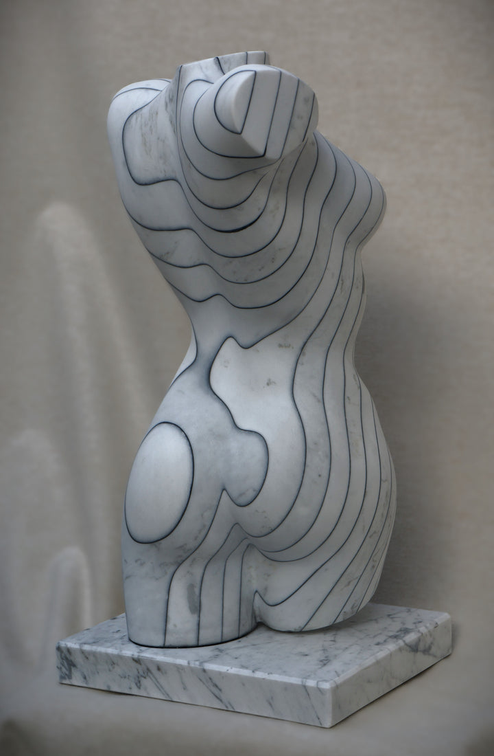Contemporary marble sculpture of a female torso featuring engraved contour-like linework, mounted on a marble base, with a smooth, polished surface and subtle grey veining.