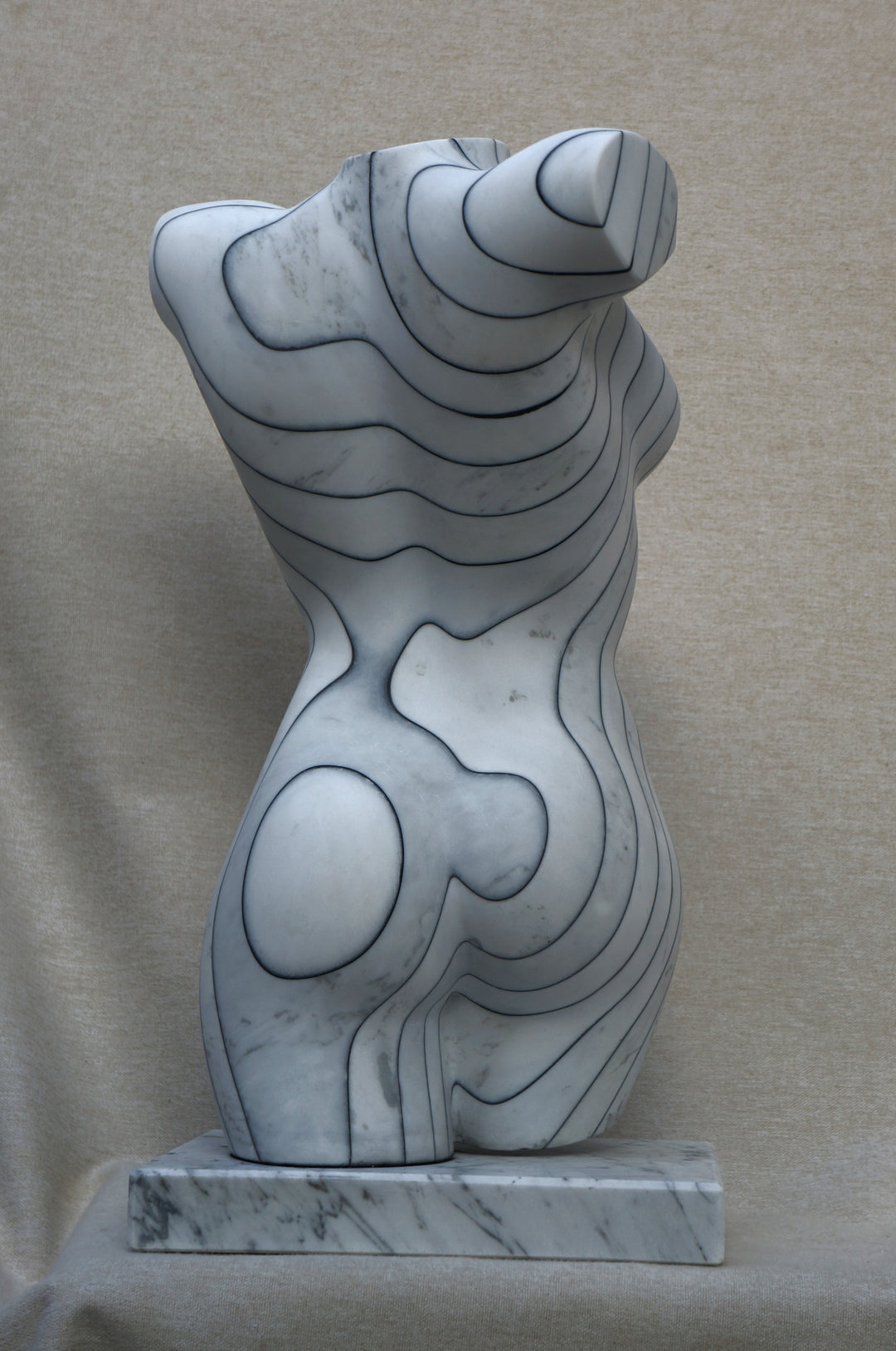 Contemporary marble sculpture of a female torso featuring engraved contour-like linework, mounted on a marble base, with a smooth, polished surface and subtle grey veining.