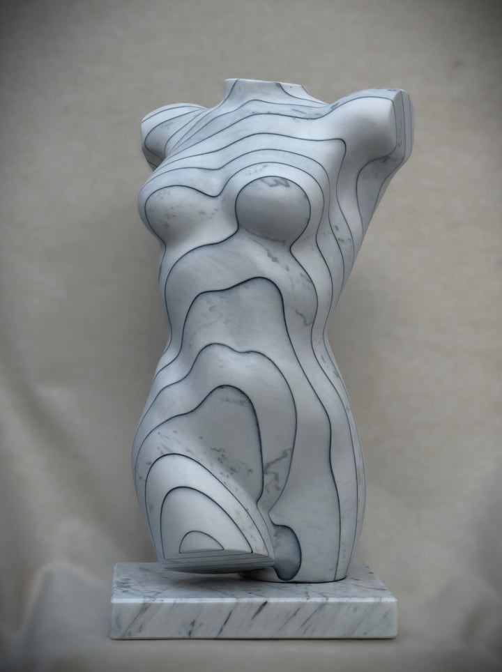 Contemporary marble sculpture of a female torso featuring engraved contour-like linework, mounted on a marble base, with a smooth, polished surface and subtle grey veining.