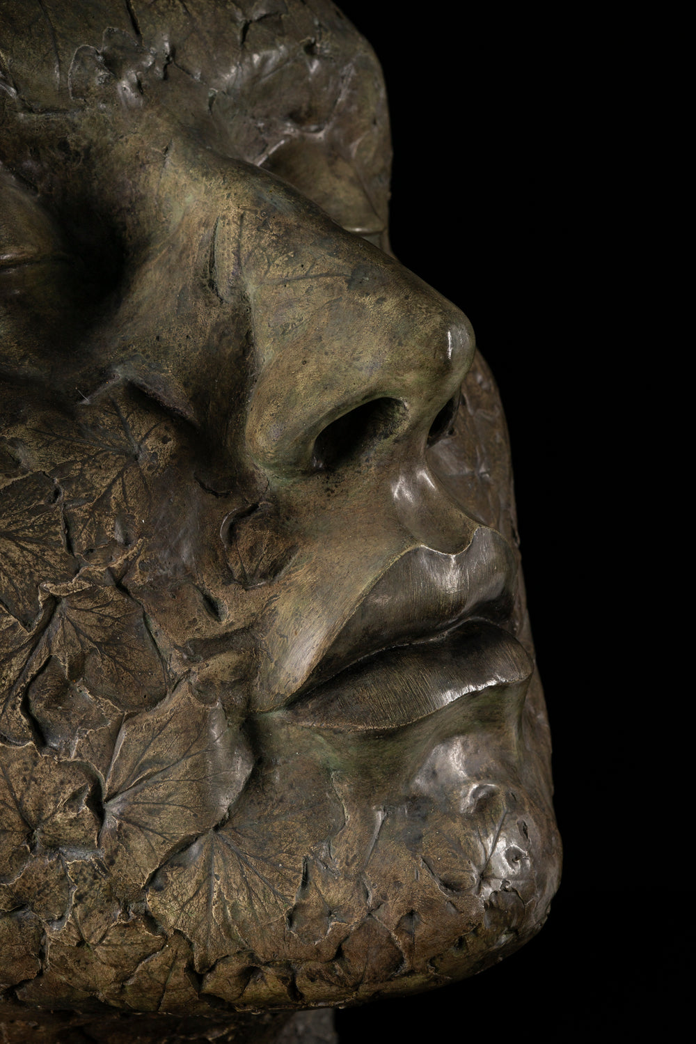 Contemplative bronze sculpture of a human face with closed eyes, tilted gently upward as if listening to the sounds of the forest. The surface is intricately detailed with embossed leaves and natural textures, merging human and woodland forms. With a rich patinated finish and mounted on a dark wooden plinth, this serene head sculpture symbolises quiet connection to nature, tree communication, and environmental awareness.