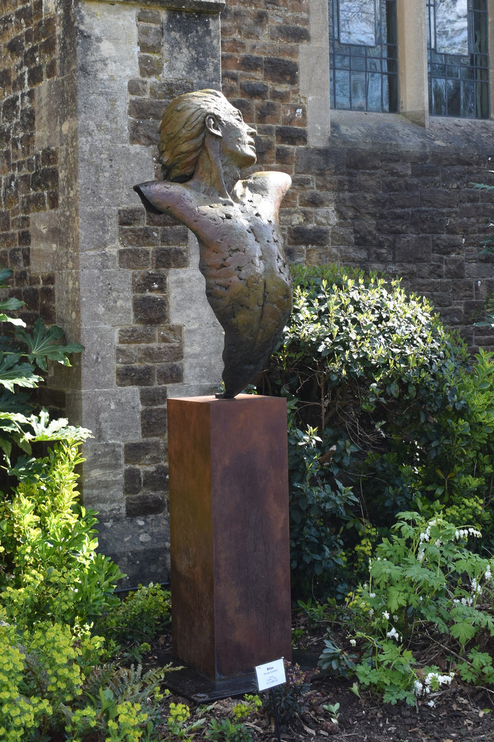 Nicola Godden Bliss Icarus bronze sculpture portraying a stylised human figure rising upward with arms extended and head turned, evoking a moment of release and quiet strength. The elongated form suggests lift and motion while remaining grounded through a solid Corten steel base. The textured bronze surface carries depth and variation, with light catching across its contours to enhance the sense of movement and presence.