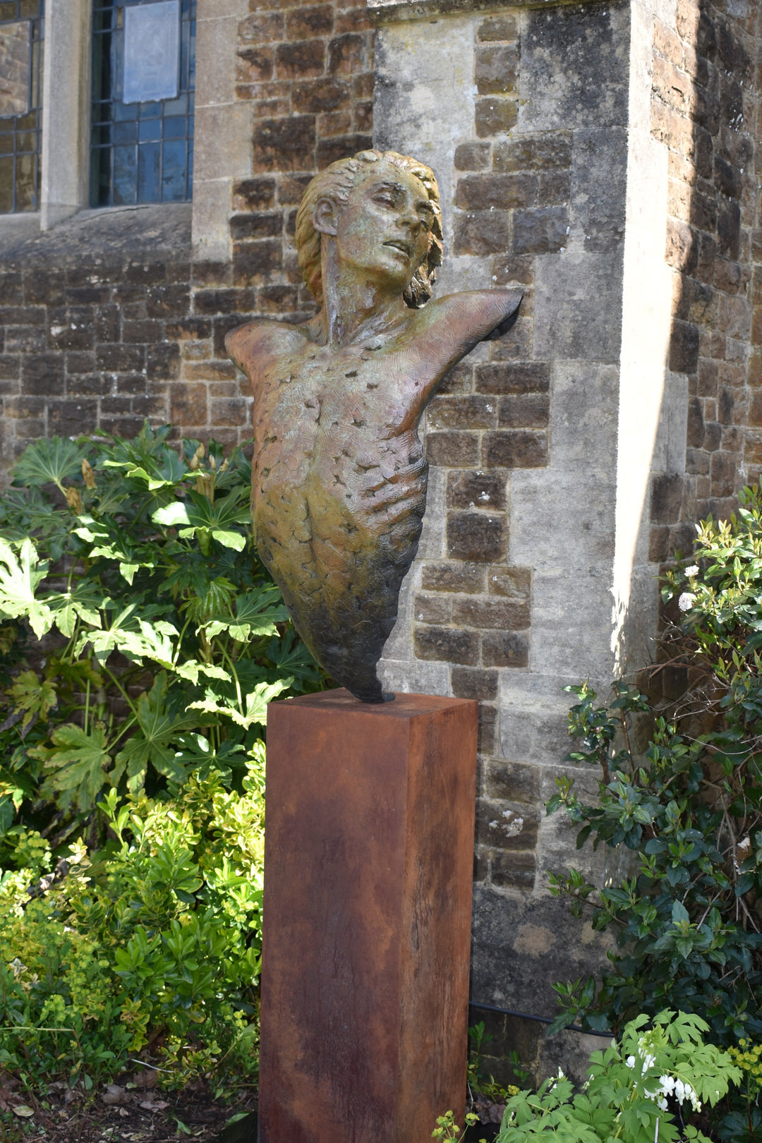 Nicola Godden Bliss Icarus bronze sculpture portraying a stylised human figure rising upward with arms extended and head turned, evoking a moment of release and quiet strength. The elongated form suggests lift and motion while remaining grounded through a solid Corten steel base. The textured bronze surface carries depth and variation, with light catching across its contours to enhance the sense of movement and presence.