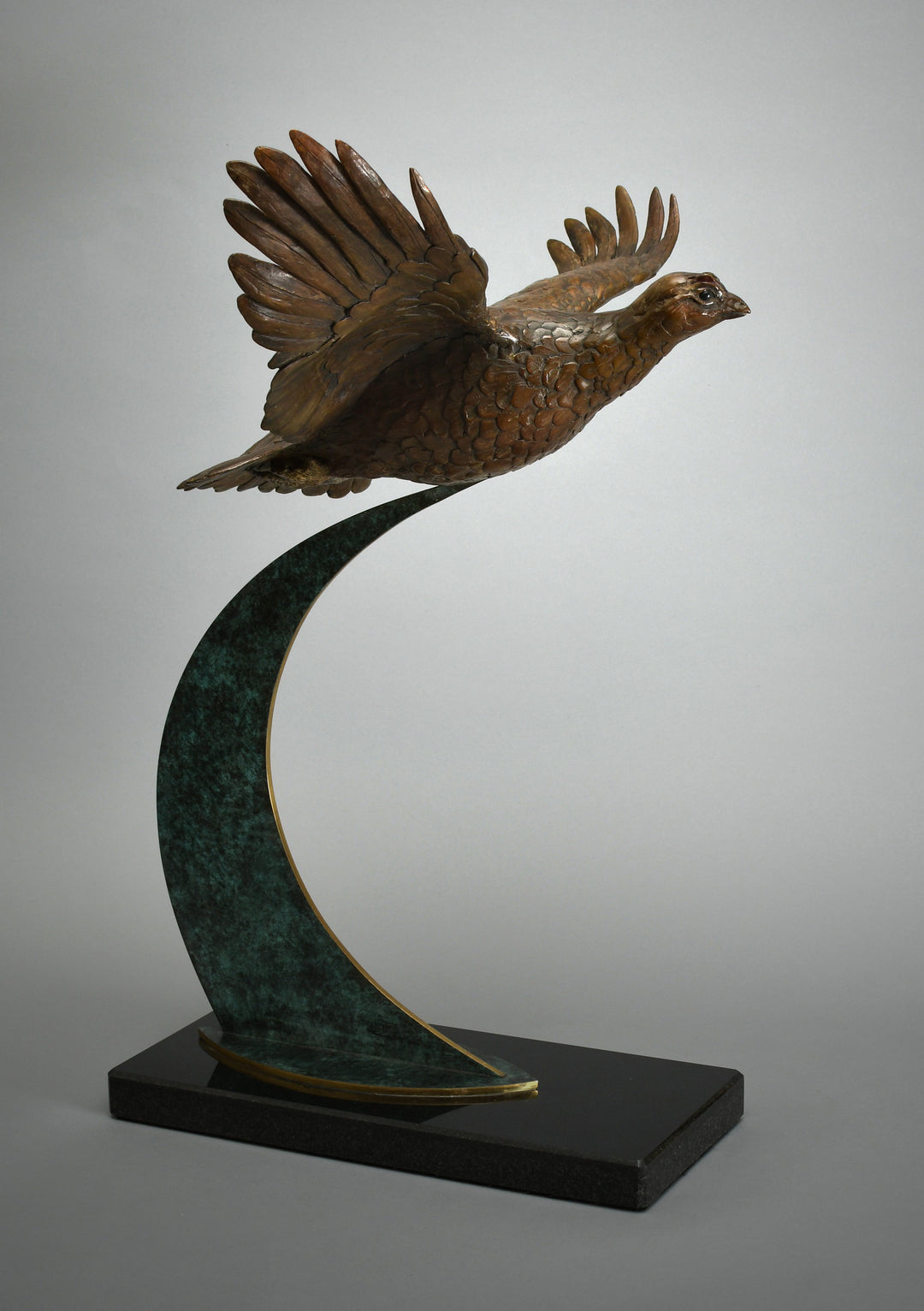 Bronze sculpture of a pheasant in full flight mounted on a sweeping green-patinated arc, fixed to a polished black base