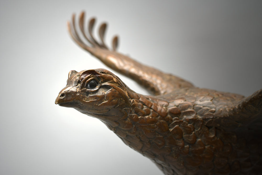 Bronze sculpture of a pheasant in full flight mounted on a sweeping green-patinated arc, fixed to a polished black base