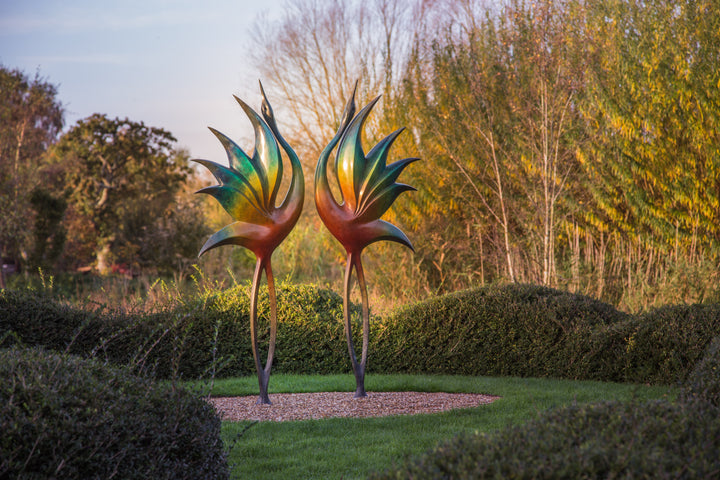 Simon Gudgeon bronze sculpture Dancing Cranes featuring elegant crane-inspired organic forms with sweeping upward curves displayed within a landscaped garden setting.