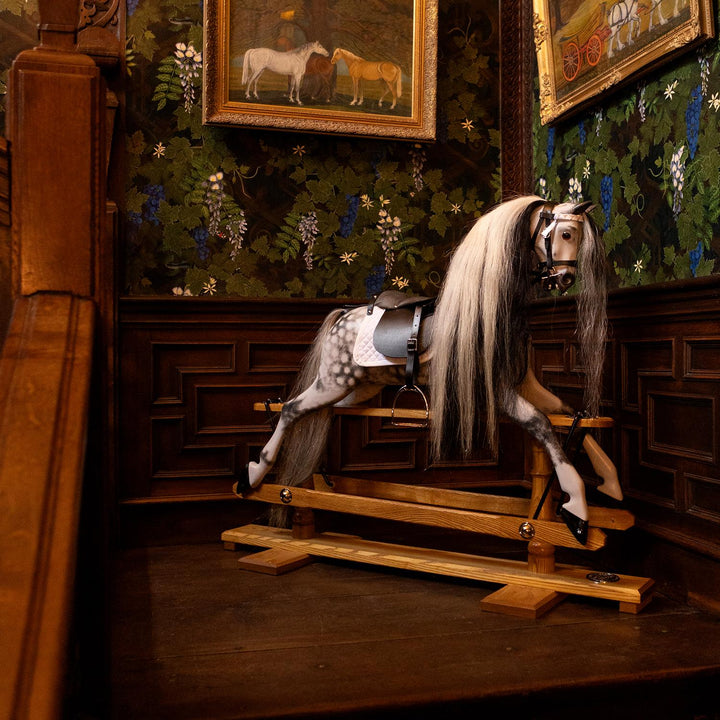 Hand-painted dapple grey rocking horse with long black and white mane, black leather saddle, and oak safety stand.

