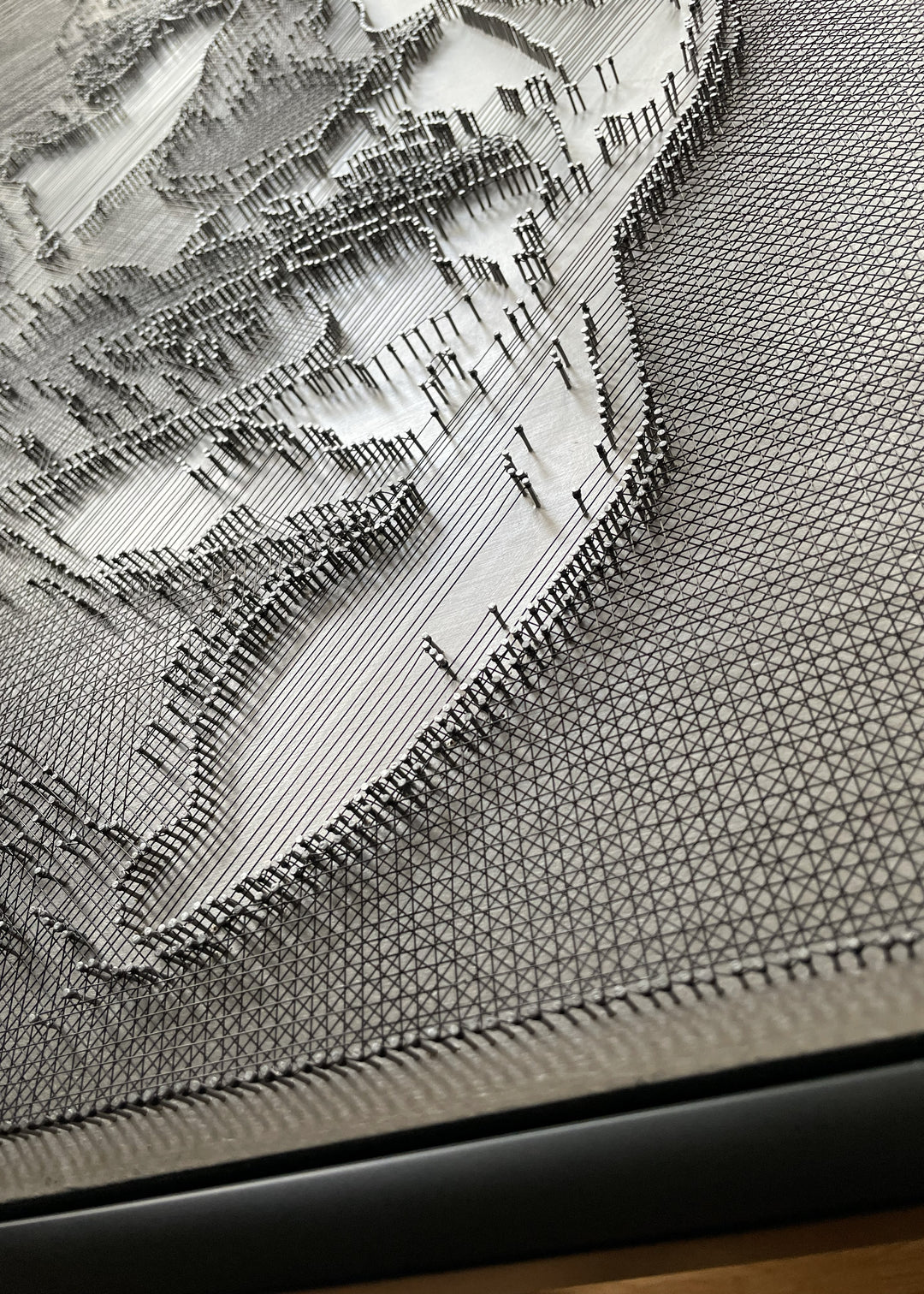 Portrait of David Bowie constructed from fine black enamelled copper wire tensioned around thousands of small metal nails on a silver acrylic painted board, forming dense linear layers that define facial features, hair and expression through tonal variation, depth and shadow across a rigid rectangular surface.