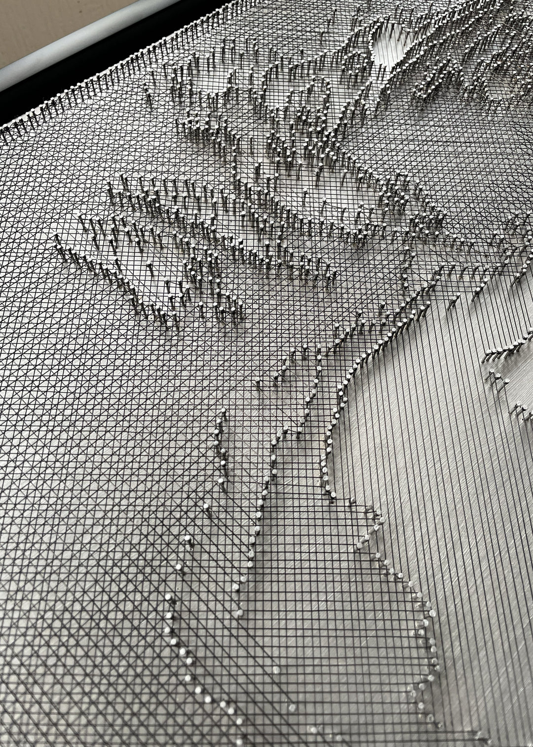 Portrait of David Bowie constructed from fine black enamelled copper wire tensioned around thousands of small metal nails on a silver acrylic painted board, forming dense linear layers that define facial features, hair and expression through tonal variation, depth and shadow across a rigid rectangular surface.
