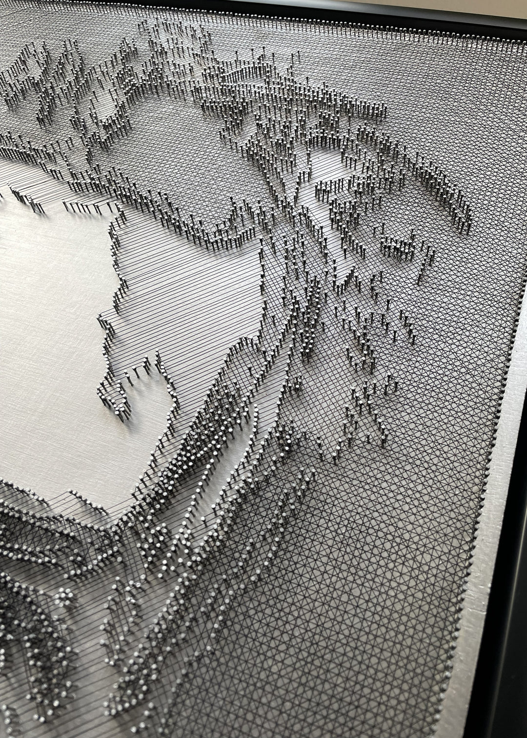 Portrait of David Bowie constructed from fine black enamelled copper wire tensioned around thousands of small metal nails on a silver acrylic painted board, forming dense linear layers that define facial features, hair and expression through tonal variation, depth and shadow across a rigid rectangular surface.