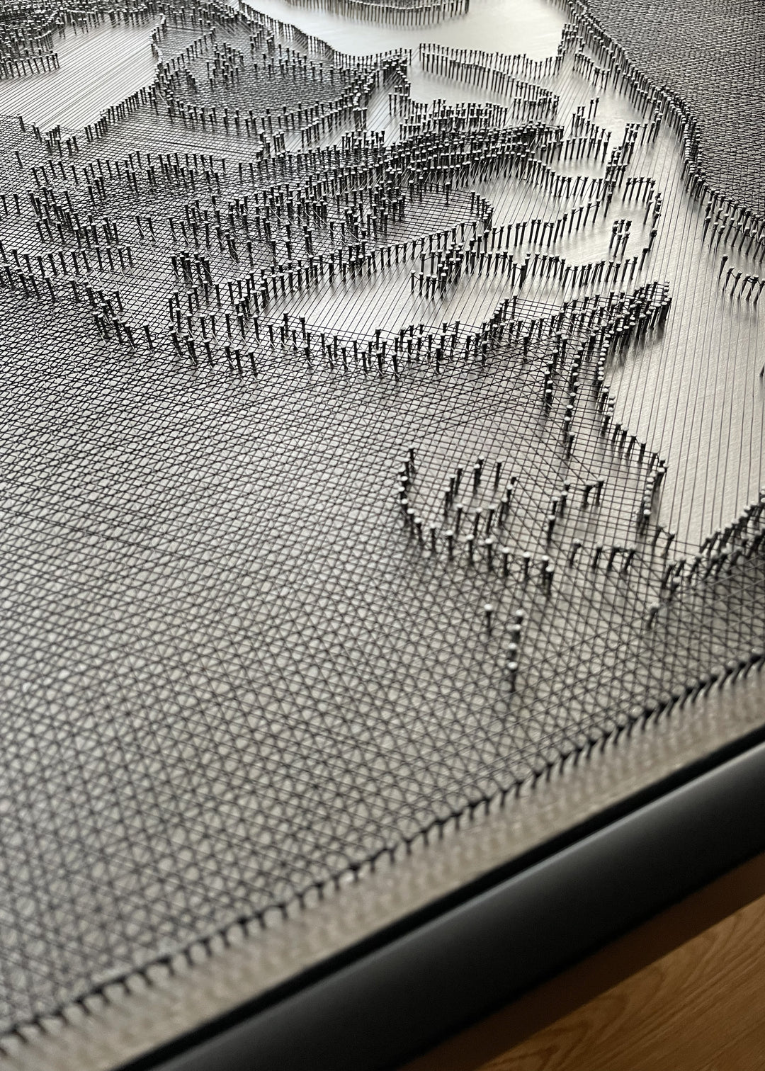 Portrait of David Bowie constructed from fine black enamelled copper wire tensioned around thousands of small metal nails on a silver acrylic painted board, forming dense linear layers that define facial features, hair and expression through tonal variation, depth and shadow across a rigid rectangular surface.
