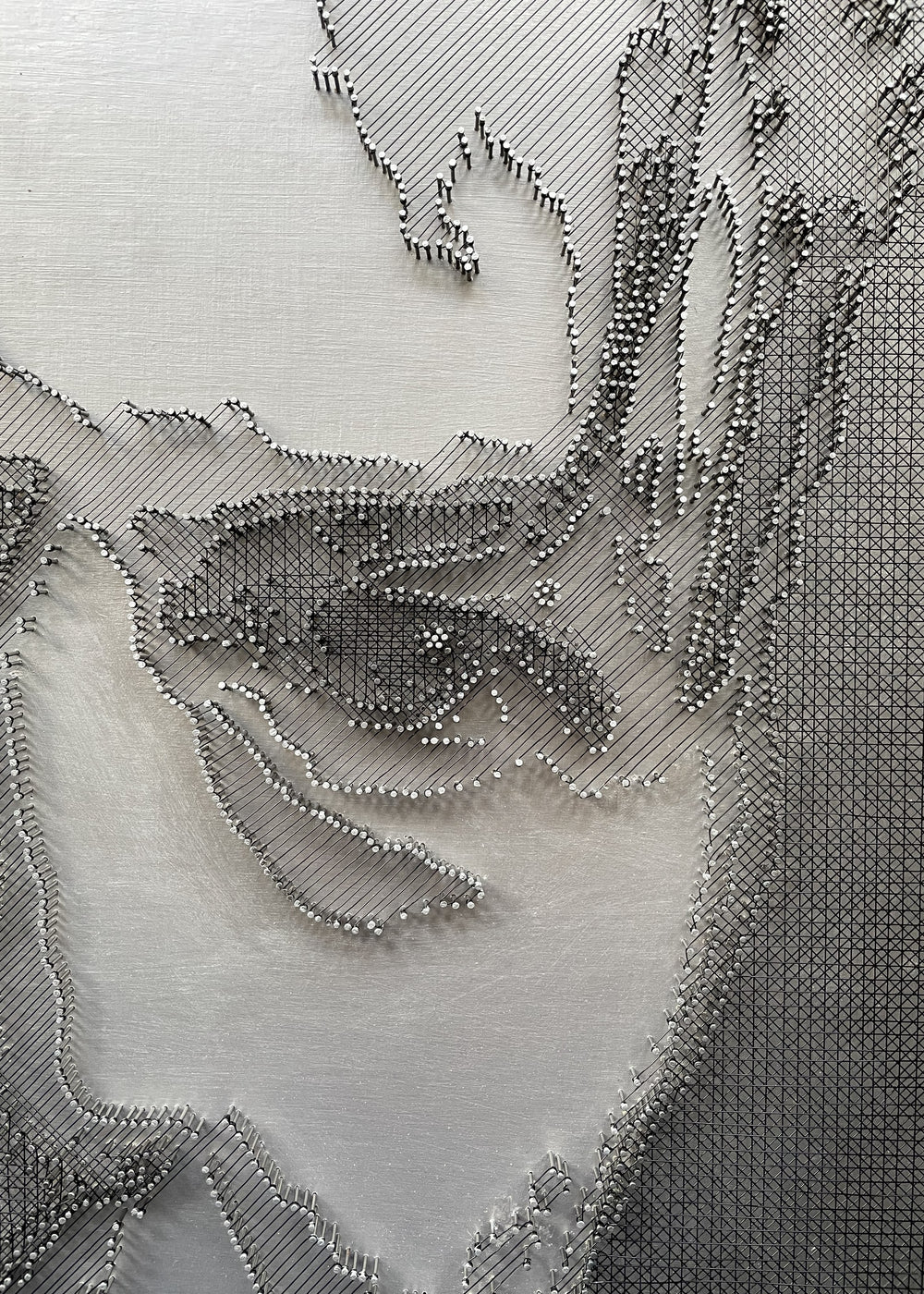 Portrait of David Bowie constructed from fine black enamelled copper wire tensioned around thousands of small metal nails on a silver acrylic painted board, forming dense linear layers that define facial features, hair and expression through tonal variation, depth and shadow across a rigid rectangular surface.