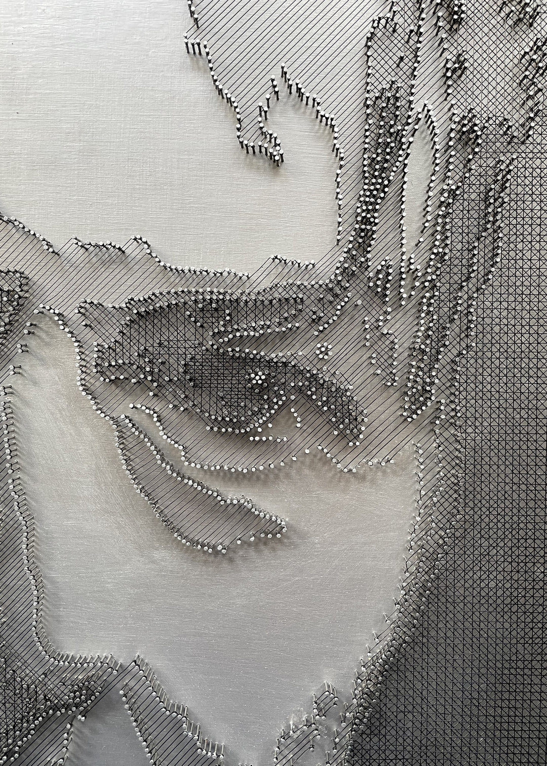 Portrait of David Bowie constructed from fine black enamelled copper wire tensioned around thousands of small metal nails on a silver acrylic painted board, forming dense linear layers that define facial features, hair and expression through tonal variation, depth and shadow across a rigid rectangular surface.