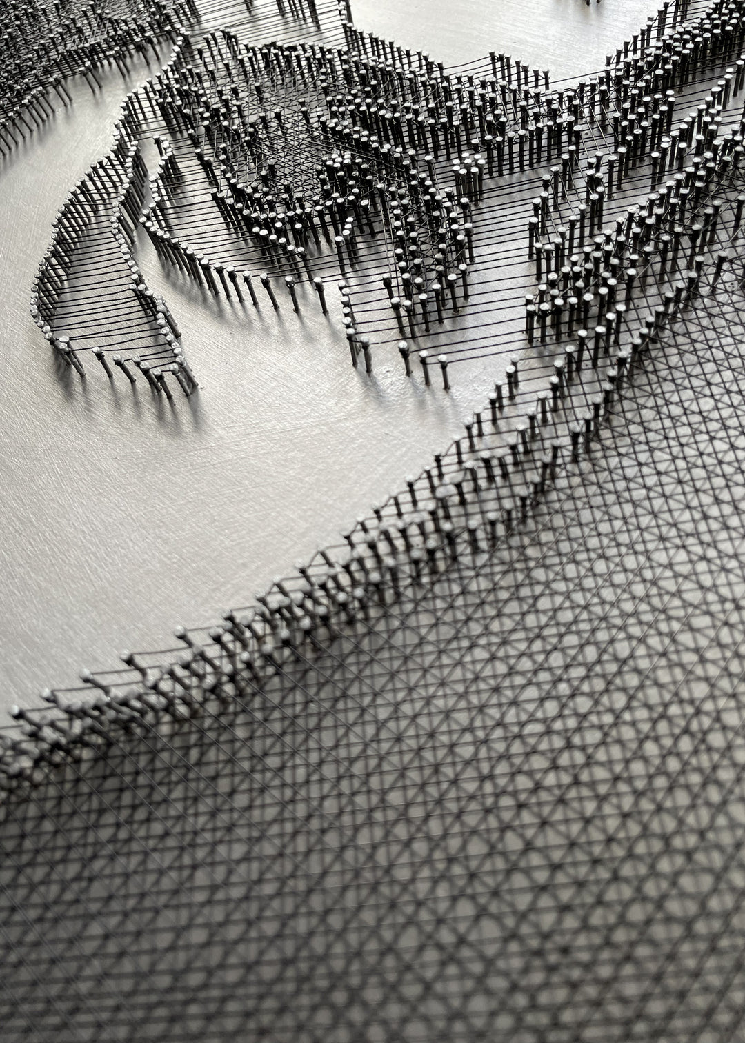 Portrait of David Bowie constructed from fine black enamelled copper wire tensioned around thousands of small metal nails on a silver acrylic painted board, forming dense linear layers that define facial features, hair and expression through tonal variation, depth and shadow across a rigid rectangular surface.