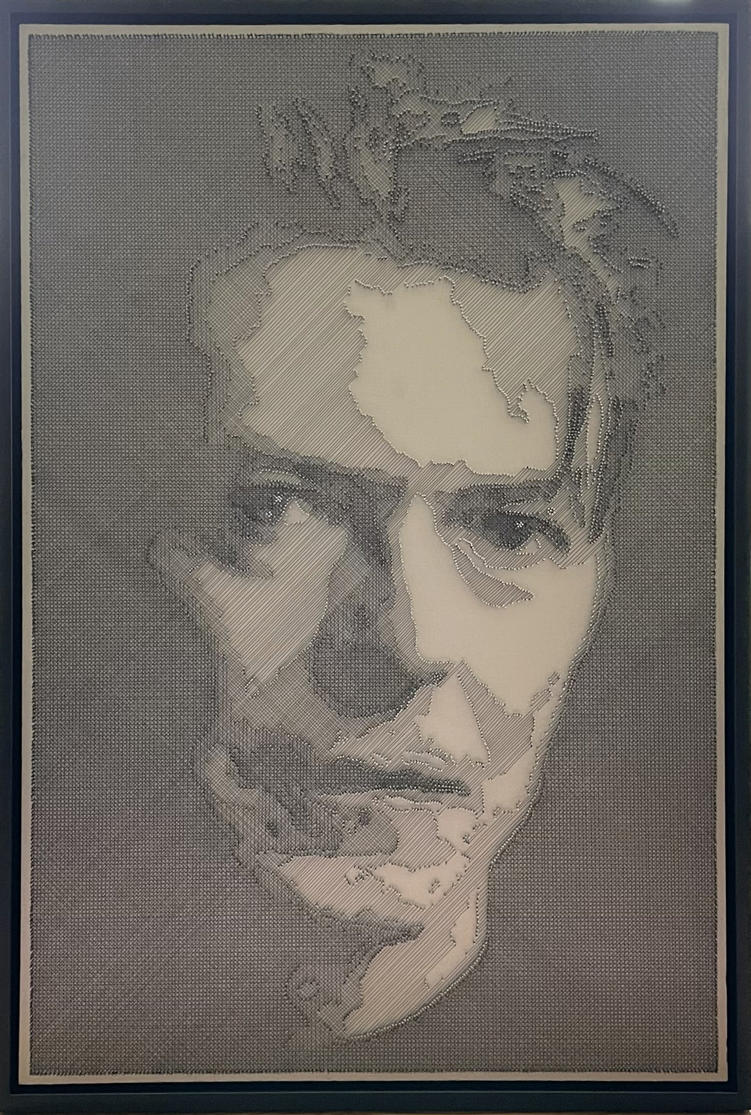 Portrait of David Bowie constructed from fine black enamelled copper wire tensioned around thousands of small metal nails on a silver acrylic painted board, forming dense linear layers that define facial features, hair and expression through tonal variation, depth and shadow across a rigid rectangular surface.